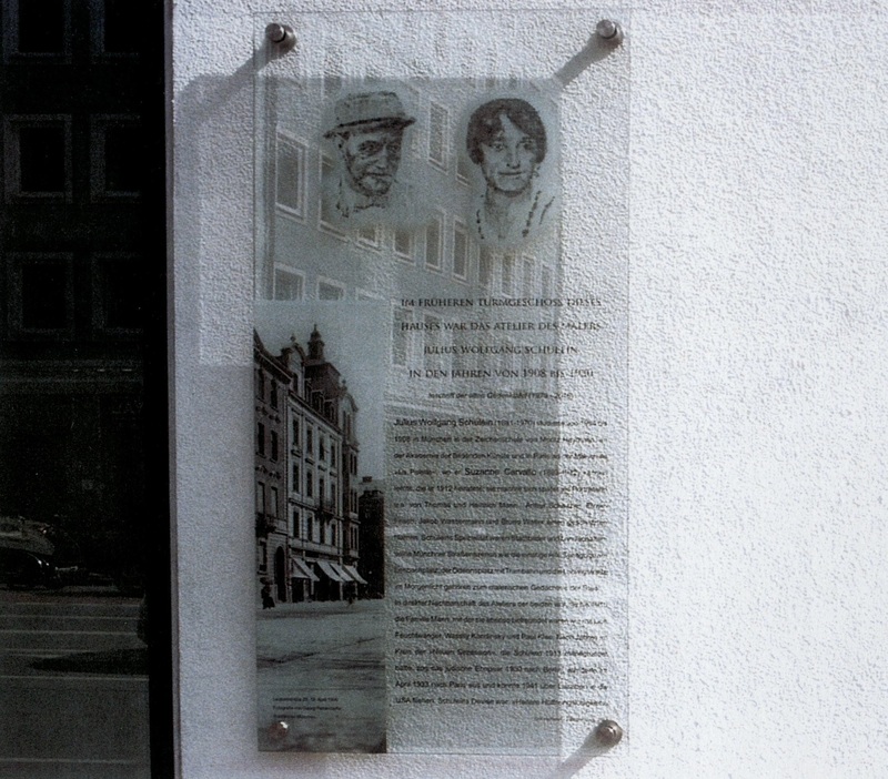 Tafel zum Gedenken an das Turmatelier des Malers Julius Wolfgang Schülein und der Malerin Suzanne Carvallo-Schülein, 2023 Im Juli 1979 wurde am Haus Leopoldstraße 2, damals im Besitz der Bayerischen Hypotheken- und Wechsel-Bank, über dem Eingang an der Leopoldstraße eine Gedenktafel aus Muschelkalk, gestaltet von Karl Oppenrieder, angebracht, um an das Atelier des Malers Julius Wolfgang Schülein im früheren Turmgeschoss des Hauses zu erinnern. Die Initiative dazu ging von der Stadt München aus, nachdem Schüleins Tochter und sein Neffe, Cathérine Hannigsberg und Werner Jacob Cahnmann, den schriftlichen Nachlass des Malers im Jahr 1974 an die Monacensia übergeben und – nach einer Ausstellung im Lenbachhaus 1973 – mit Münchner Museen über den Ankauf und die Stiftung von Bildern verhandelt hatten. Im Sommer 2016 wurde die Tafel bei Baumaßnahmen nach einem Besitzerwechsel der Häuser Franz-Joseph-Straße 2 und Leopoldstraße 21 entfernt, auf Initiative des neuen Eigentümers aber 2021 in Form einer Glastafel neugestaltet. Digitaldruck auf Glas nach Porträt-Gouachen von Joachim Jung und einer Fotografie von Georg Pettenkofer. Text: Dirk Heißerer. Erstellt von: Joachim Jung