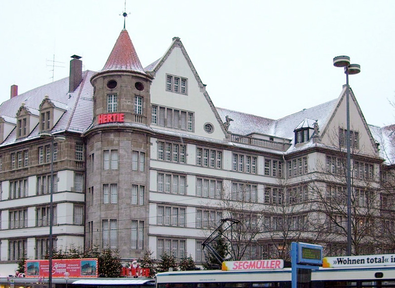 Die Fassade des Kaufhauses Hertie, 2005 Nach der Übernahme von Hertie durch die Karstadt AG 1994 wurde das Haus bis 2007 unter diesem Namen geführt, dann in Karstadt München Bahnhofplatz umbenannt. Mehrfach wechselte das Anwesen danach den Besitzer, bis es 2017 vom österreichischen Unternehmer René Benko übernommen und nach dessen Insolvenz 2023 geschlossen wurde. Seither stagniert der Umbau, und neue Investoren werden gesucht. Quelle: Wikimedia Commons Erstellt von: Okfm Datum: 22.12.2005